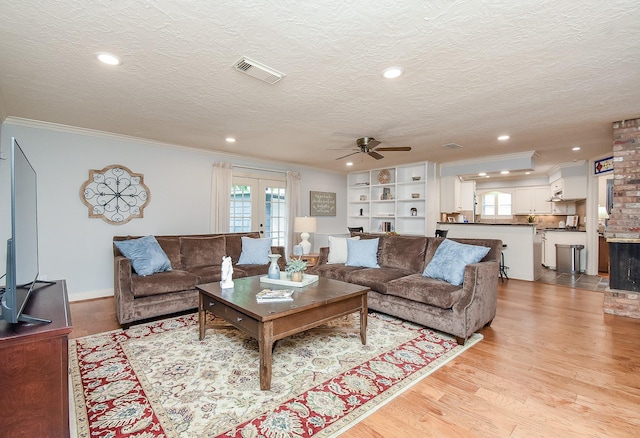 living room with french doors, a textured ceiling, light wood-type flooring, and ornamental molding