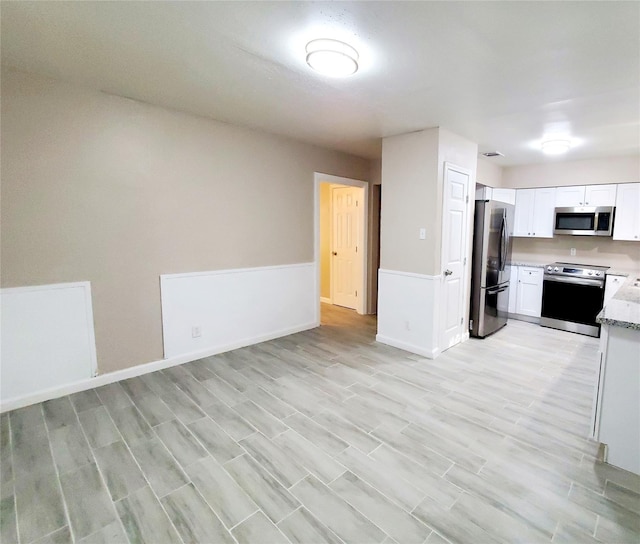 kitchen with white cabinets, light hardwood / wood-style flooring, light stone counters, and appliances with stainless steel finishes