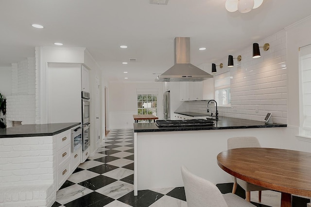 kitchen with kitchen peninsula, appliances with stainless steel finishes, island range hood, and white cabinetry