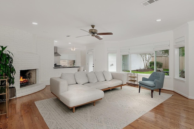 living room featuring a brick fireplace, ceiling fan, hardwood / wood-style flooring, and crown molding