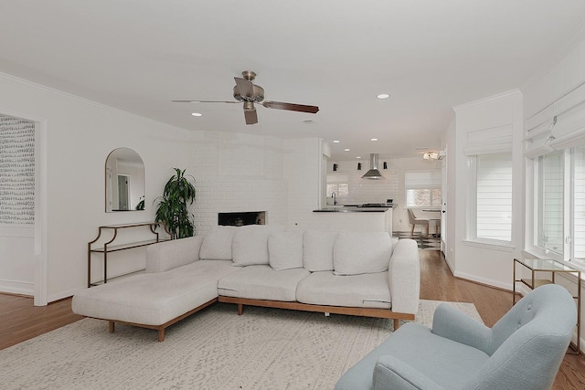 living room featuring sink, light wood-type flooring, ceiling fan, ornamental molding, and a large fireplace