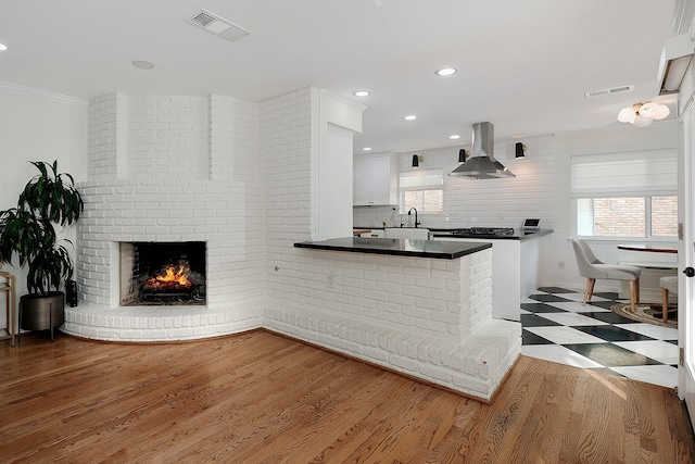 kitchen with a fireplace, white cabinetry, tasteful backsplash, hardwood / wood-style flooring, and island range hood