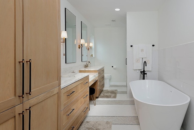 bathroom featuring tile patterned flooring, tile walls, toilet, a tub to relax in, and vanity