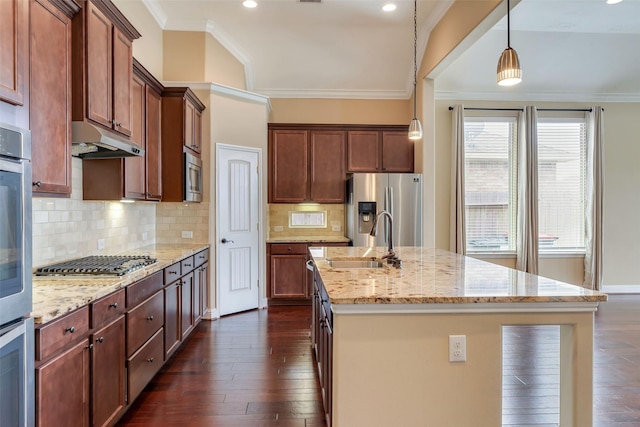 kitchen with light stone counters, hanging light fixtures, stainless steel appliances, an island with sink, and sink