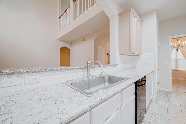 kitchen with sink, light stone counters, an inviting chandelier, dishwasher, and white cabinets