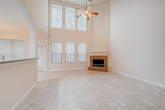 unfurnished living room with a brick fireplace, a towering ceiling, and ceiling fan