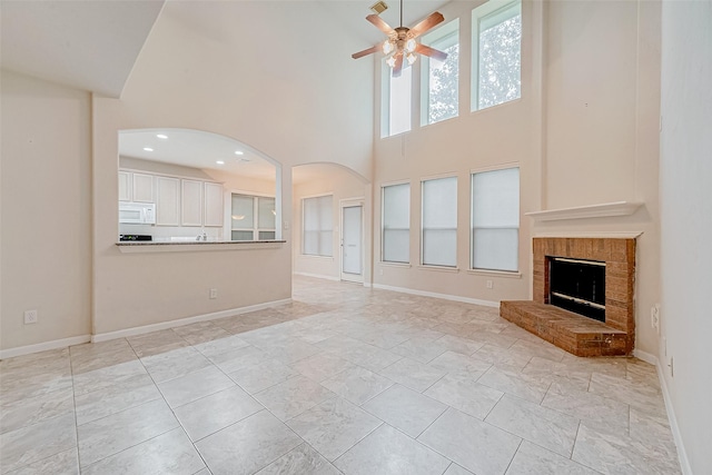 unfurnished living room featuring a towering ceiling, a fireplace, and ceiling fan