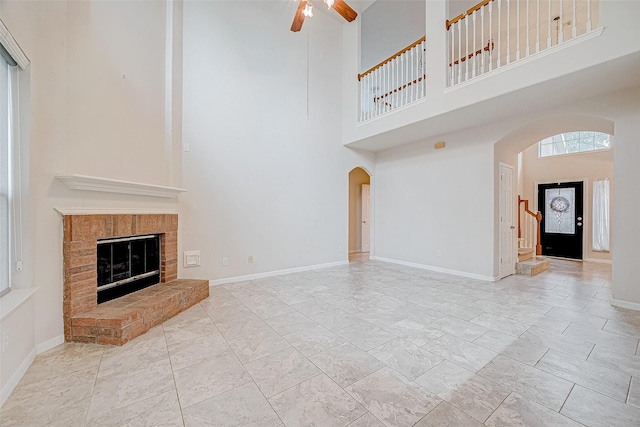 unfurnished living room with ceiling fan, a towering ceiling, and a fireplace