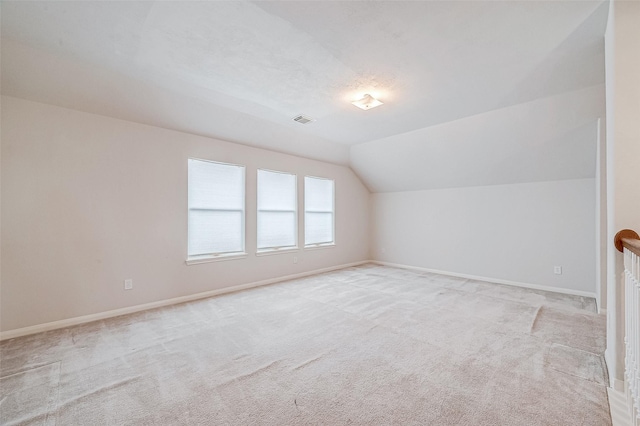 additional living space featuring lofted ceiling, light carpet, and a textured ceiling