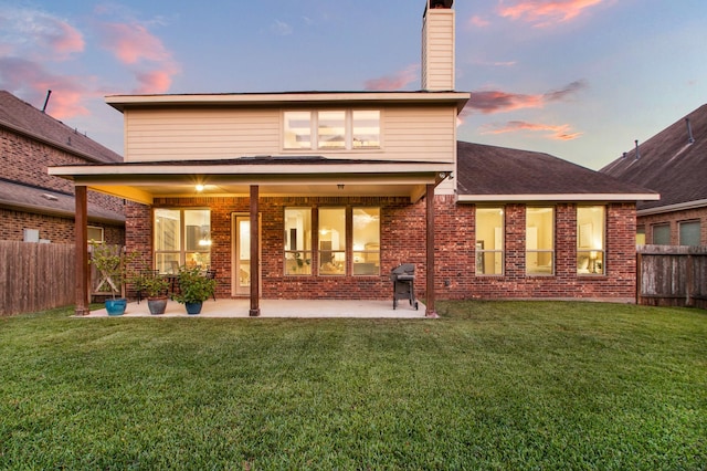 back house at dusk featuring a patio and a yard