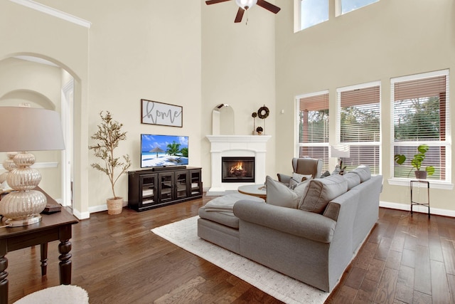 living room with a towering ceiling, dark hardwood / wood-style flooring, ceiling fan, and ornamental molding