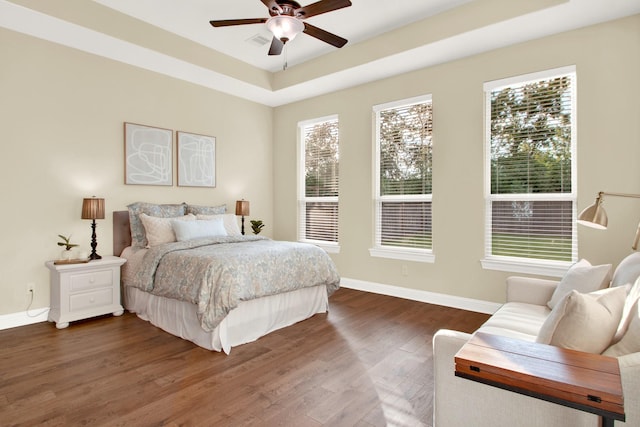 bedroom with ceiling fan, a tray ceiling, and dark wood-type flooring