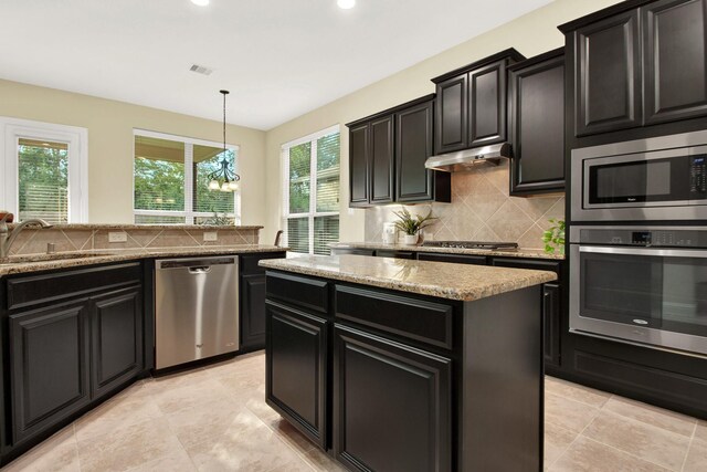 kitchen with decorative light fixtures, a kitchen island, an inviting chandelier, appliances with stainless steel finishes, and sink