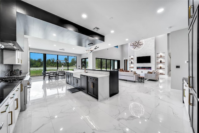 kitchen featuring wall chimney exhaust hood, sink, a center island with sink, a fireplace, and white cabinets