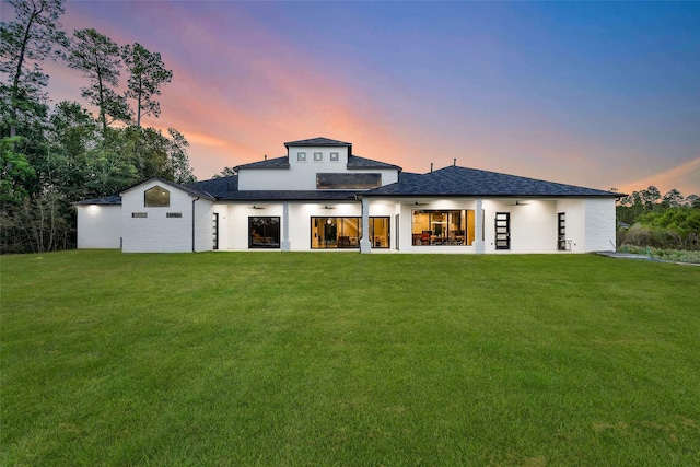 back house at dusk featuring a lawn