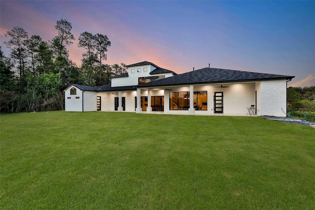 back house at dusk with a patio, a yard, and ceiling fan