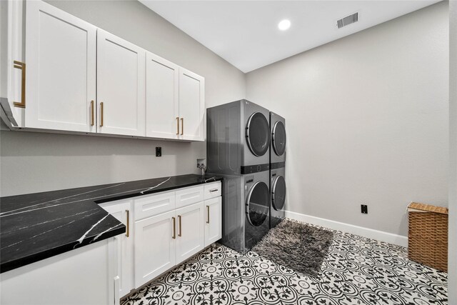 laundry room featuring light tile patterned floors, stacked washer and clothes dryer, and cabinets