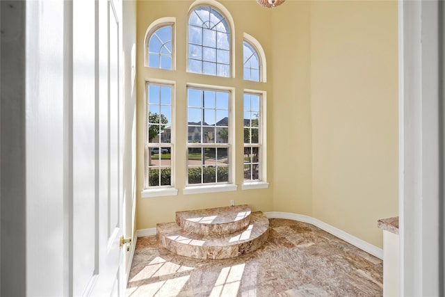 interior space featuring a healthy amount of sunlight, a towering ceiling, and baseboards