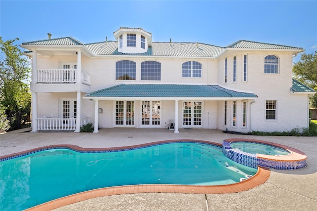 rear view of property featuring french doors, a pool with connected hot tub, a patio area, a balcony, and a tiled roof