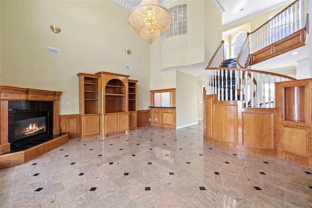 unfurnished living room with ornamental molding, a glass covered fireplace, visible vents, and a notable chandelier