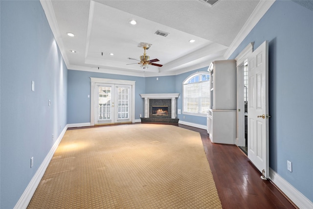 unfurnished living room featuring a ceiling fan, visible vents, baseboards, a lit fireplace, and a raised ceiling