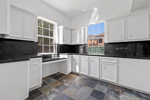 kitchen with stone finish flooring, dark countertops, white cabinetry, and decorative backsplash