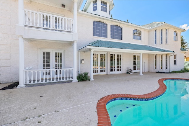 back of property with french doors, brick siding, a patio, a balcony, and an outdoor pool