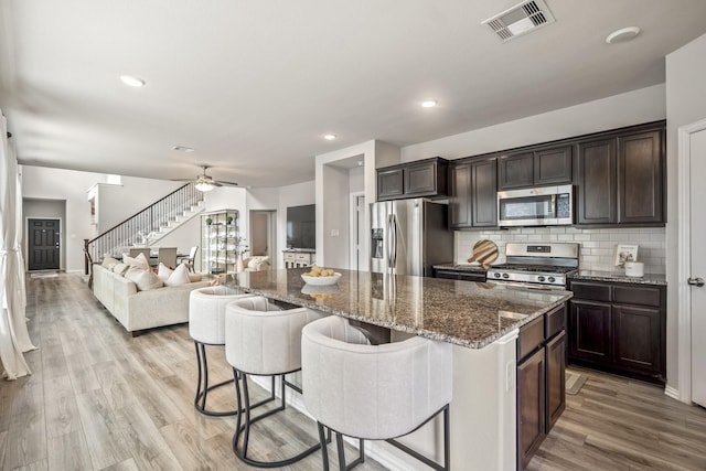 kitchen featuring a breakfast bar area, appliances with stainless steel finishes, decorative backsplash, a kitchen island, and dark brown cabinets