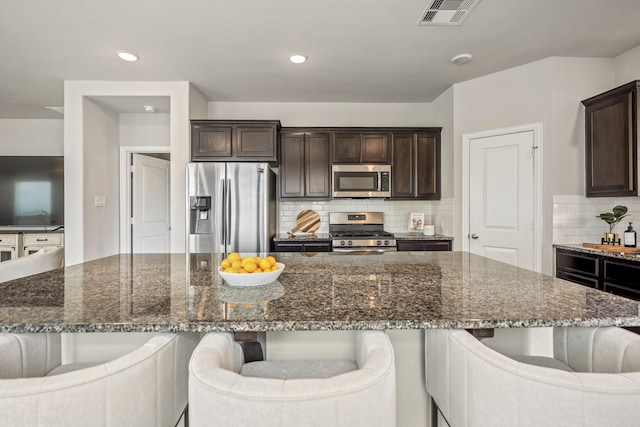 kitchen featuring a kitchen breakfast bar, dark stone countertops, stainless steel appliances, a spacious island, and dark brown cabinets