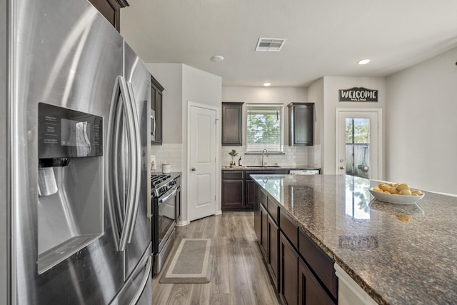 kitchen featuring light hardwood / wood-style floors, stainless steel appliances, dark stone counters, decorative backsplash, and dark brown cabinetry