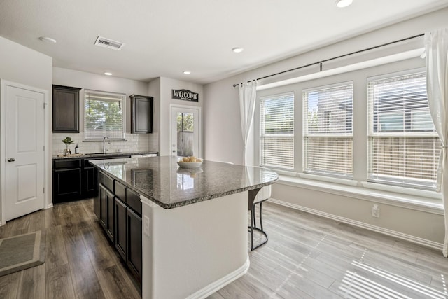 kitchen featuring sink, a breakfast bar area, decorative backsplash, dark stone counters, and a kitchen island