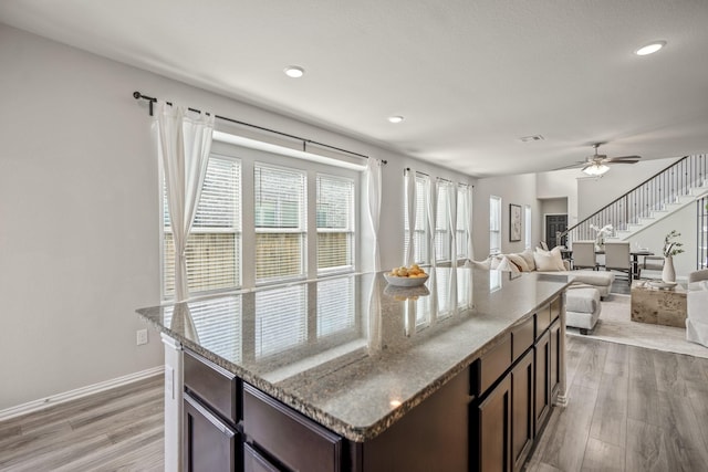 kitchen featuring light stone countertops, ceiling fan, light hardwood / wood-style floors, and dark brown cabinets