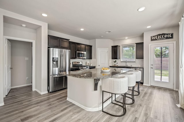 kitchen featuring stainless steel appliances, a kitchen island, backsplash, stone counters, and dark brown cabinetry