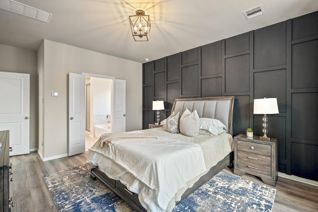 bedroom featuring wood-type flooring, connected bathroom, and a notable chandelier