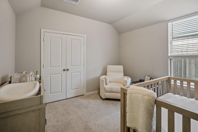 bedroom featuring light colored carpet, vaulted ceiling, a closet, and a nursery area