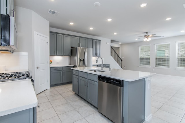 kitchen featuring an island with sink, gray cabinets, backsplash, appliances with stainless steel finishes, and sink