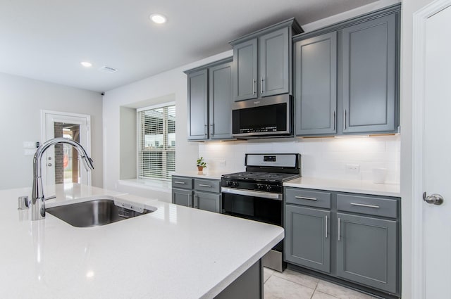 kitchen featuring tasteful backsplash, appliances with stainless steel finishes, gray cabinets, light countertops, and a sink