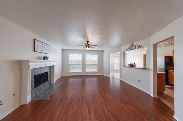 unfurnished living room with a tiled fireplace, ceiling fan, and dark hardwood / wood-style floors