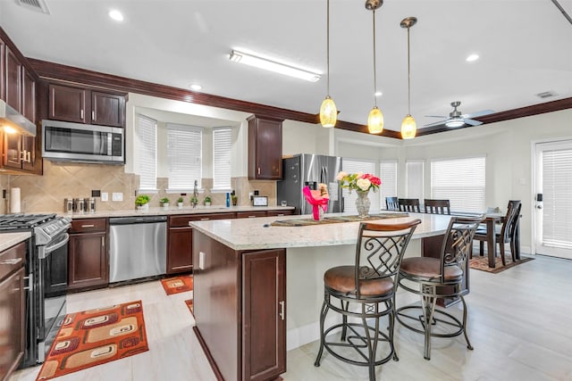 kitchen with ceiling fan, stainless steel appliances, light stone countertops, pendant lighting, and a center island