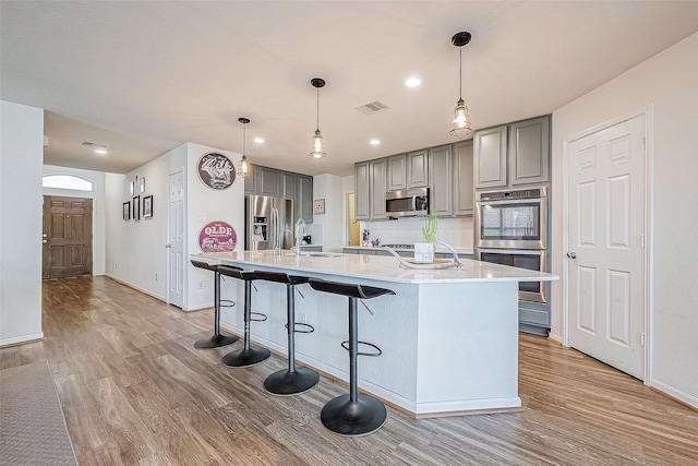 kitchen with appliances with stainless steel finishes, light hardwood / wood-style floors, gray cabinets, and a kitchen island with sink