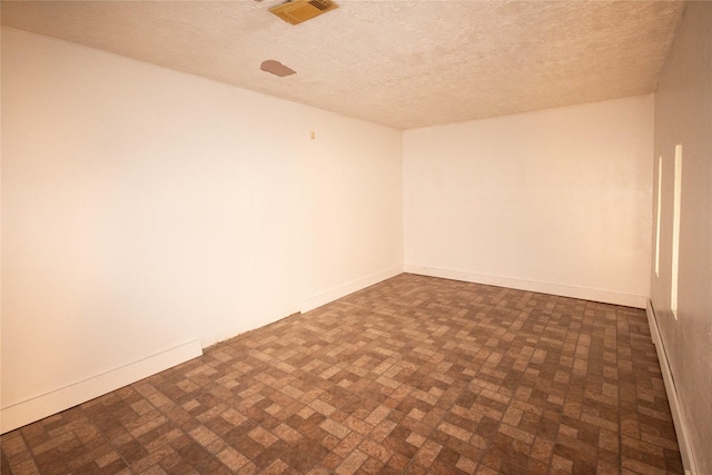 spare room featuring baseboards, brick patterned floor, visible vents, and a textured ceiling