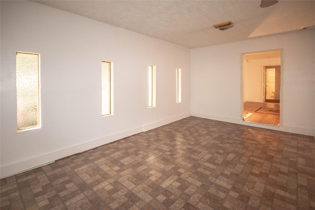 spare room featuring brick floor, a textured ceiling, and baseboards