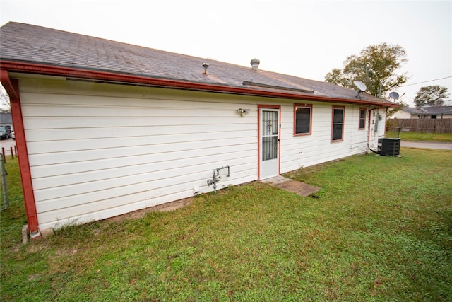 rear view of property featuring central AC, a shingled roof, a lawn, and fence