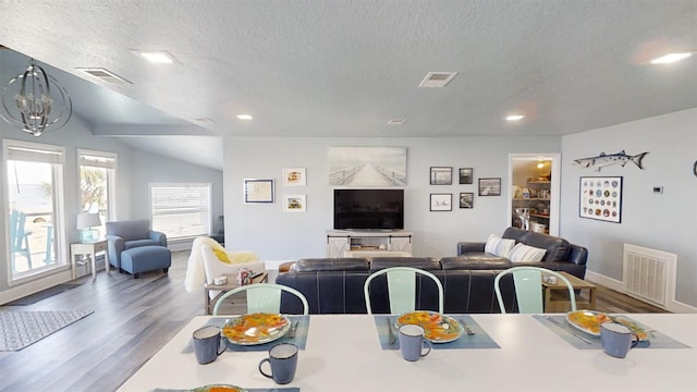 dining area with hardwood / wood-style flooring, lofted ceiling, a chandelier, and a textured ceiling