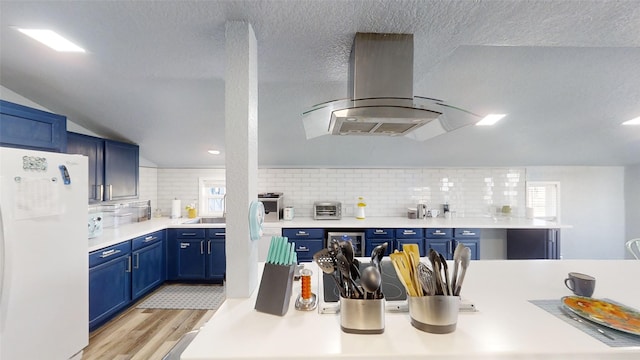 kitchen with island exhaust hood, white refrigerator, tasteful backsplash, light hardwood / wood-style floors, and blue cabinets