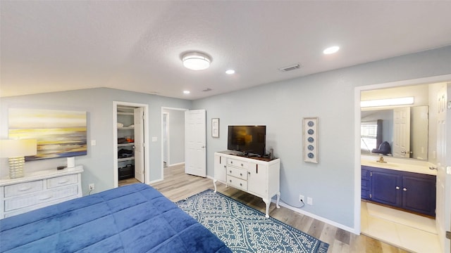 bedroom featuring ensuite bath, lofted ceiling, a walk in closet, light hardwood / wood-style floors, and a textured ceiling