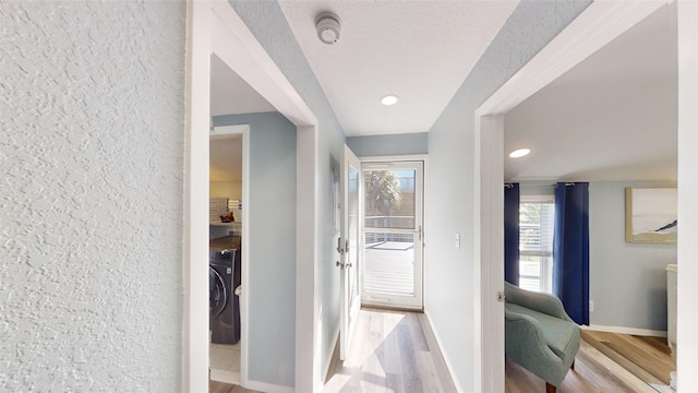 corridor with washer / clothes dryer, a textured ceiling, and light wood-type flooring