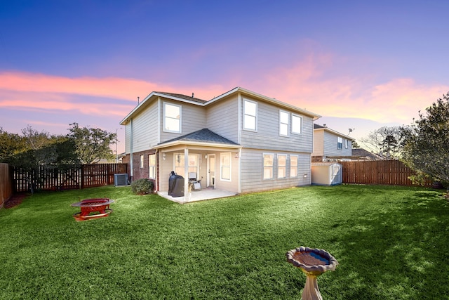 back house at dusk with a patio, cooling unit, an outdoor fire pit, and a lawn