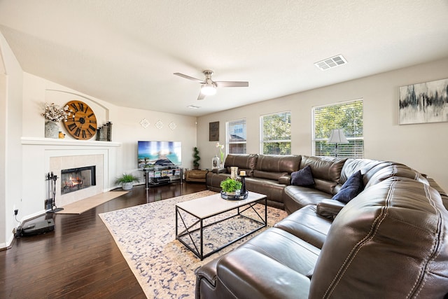 living room featuring a tiled fireplace, dark wood-type flooring, a textured ceiling, and ceiling fan