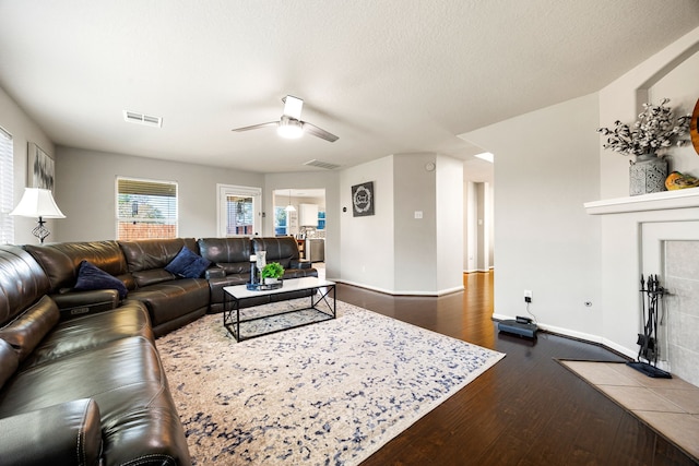 living room featuring a tile fireplace, dark wood-type flooring, and ceiling fan